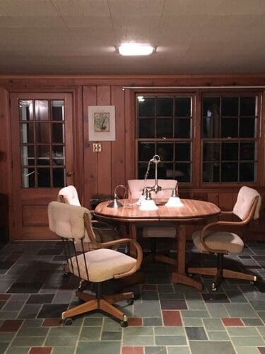 Cozy wooden dining room with a round table and four comfortable upholstered chairs, illuminated by a ceiling light; perfect for intimate gatherings and family meals.