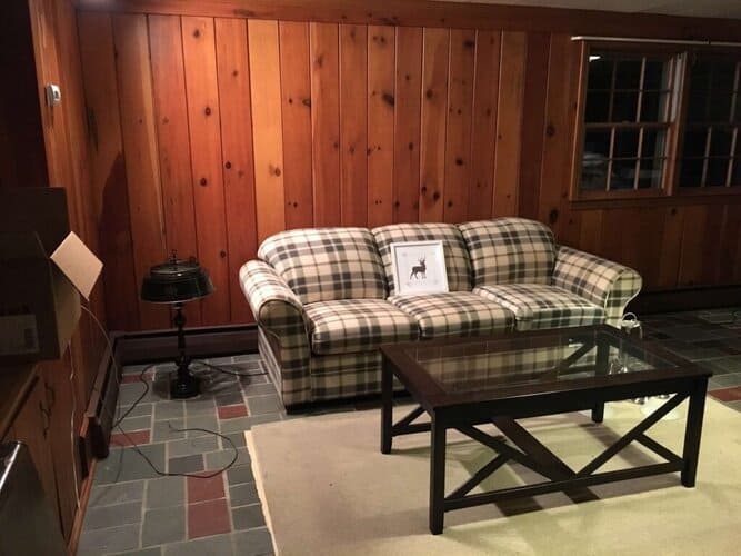 Dated plaid sofa in cozy wood-paneled living room with rustic decor and wooden flooring.