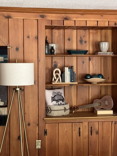 Rustic wooden bookshelf with decorative vases, a cozy throw blanket, a small guitar, and books, creating a warm and inviting home decor setup in a modern living space.