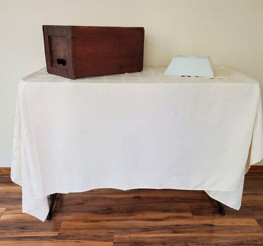 Wooden wine box on white table with cloth covering, indoor setting, minimal decor, creating a cozy and rustic ambiance.