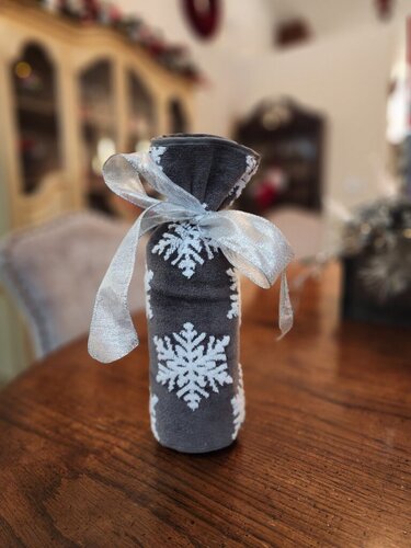 Wine bottle wrapped in holiday dish towel featuring snowflakes and decorative ribbon.